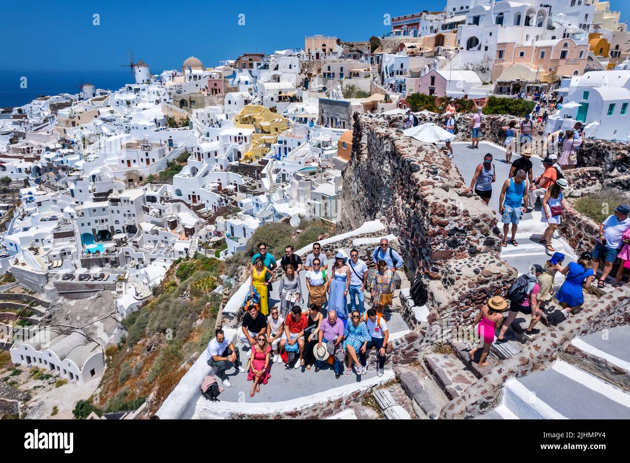 Gruppe von Touristen, die sich mit einem Teil des Dorfes Oia im Hintergrund ausruhen. Santorini, Kykladen, Ägäis, Griechenland. Stockfoto