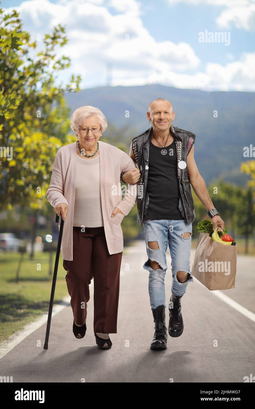 Mann, der einer älteren Frau mit einem Gehstock hilft und eine Einkaufstasche im Freien trägt Stockfoto