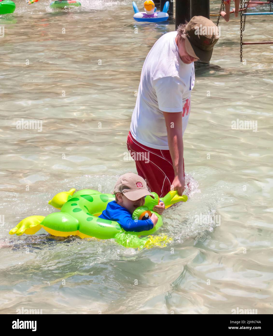 Mann und kleiner Junge mit Froschschwimmrohr, die sich im Schwimmbad abkühlen Stockfoto