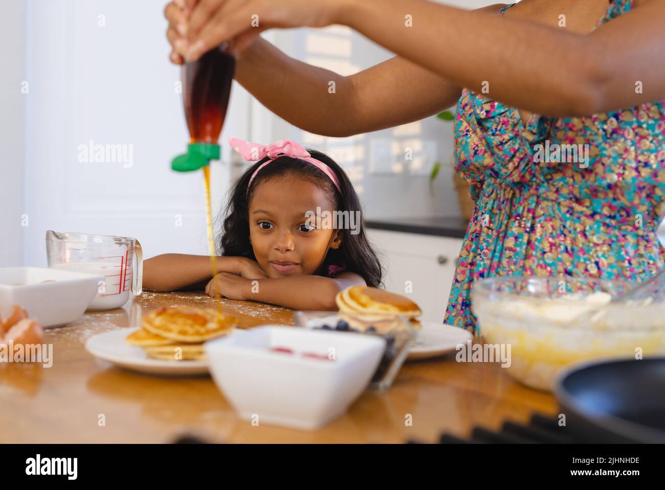 Mittelteil von biracial aufgeregt Mädchen Blick auf verlockende Pfannkuchen und Mutter gießt Honig darauf Stockfoto