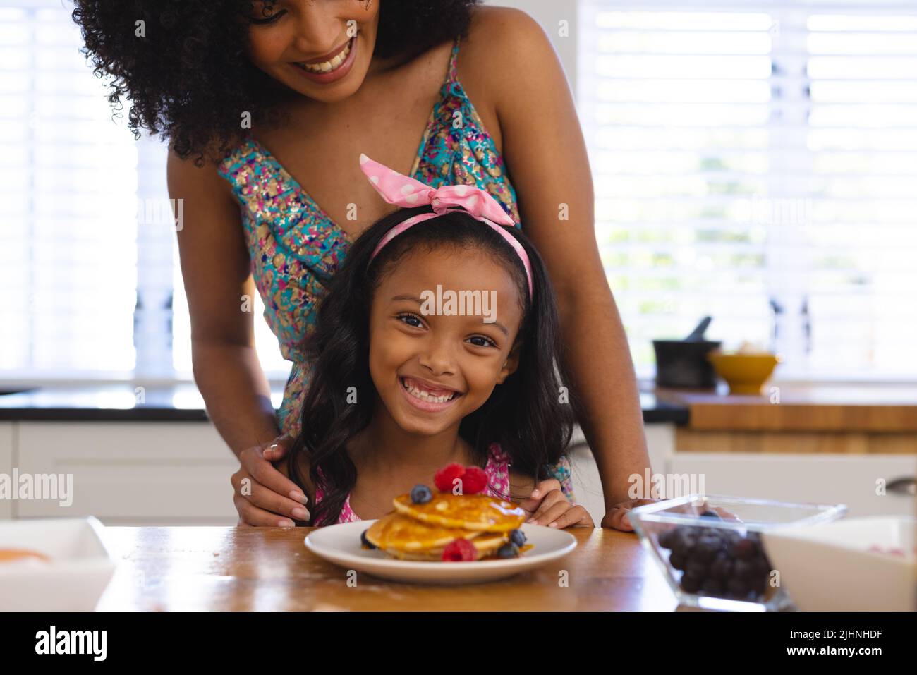 Mittelteil von glücklicher Birazialmutter und Tochter mit verlockenden Pfannkuchen auf dem Tisch zu Hause Stockfoto