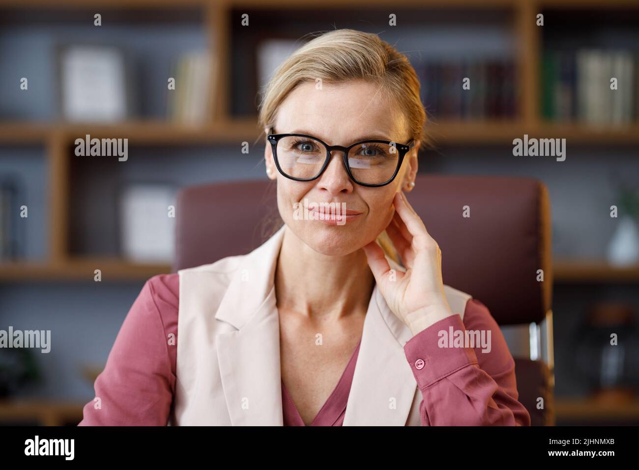 Porträt einer schönen blondie Frau, die die Kamera anschaut und lächelt. Erwachsene stilvolle selbstbewusste Geschäftsfrau trägt Brillen sitzen am Arbeitsplatz in Stockfoto