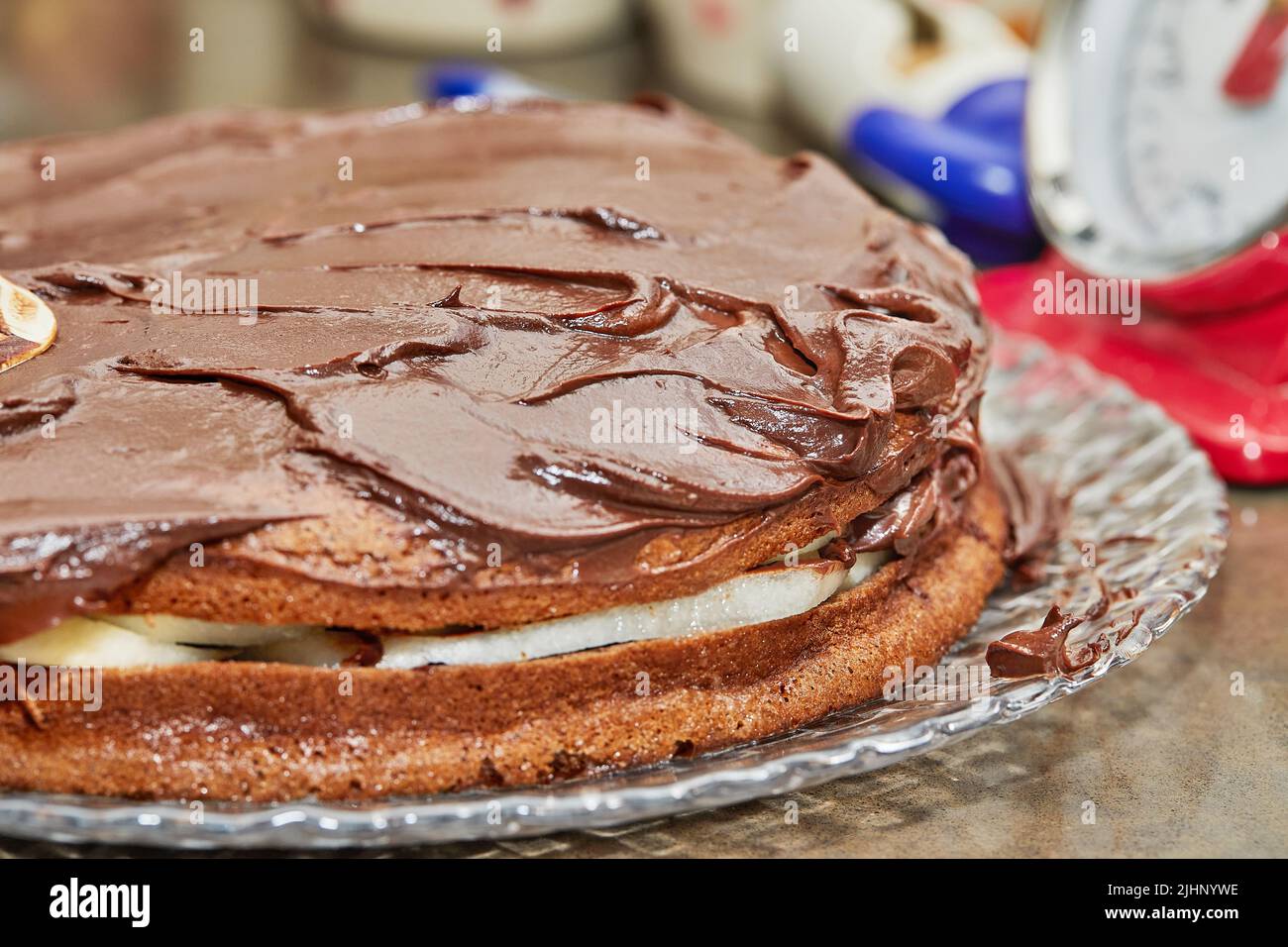 Der Koch überzieht den Kuchen mit Schokoladenganache, um Schokoladenkuchen mit Birnen und Walnüssen zu machen Stockfoto