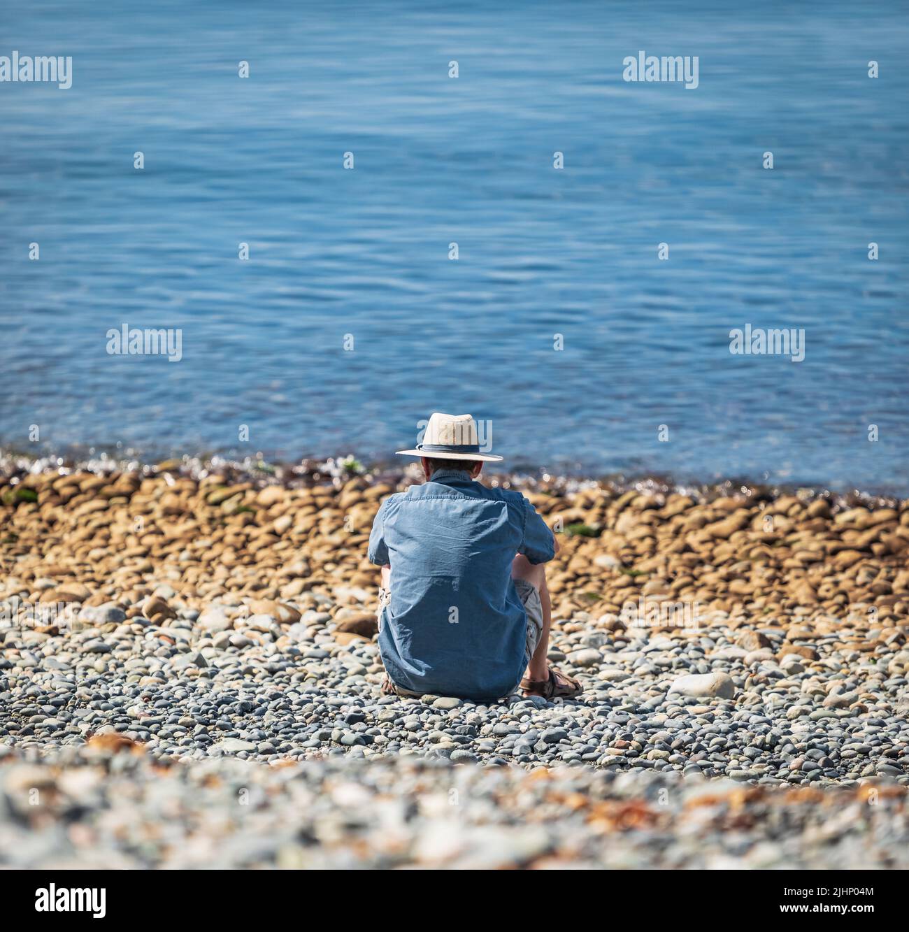Mann genießt am Strand an einem Sommertag im Urlaub. Mann im Hut, der sich an einem sonnigen Tag am Strand entspannt. Reisefoto, selektiver Fokus Stockfoto