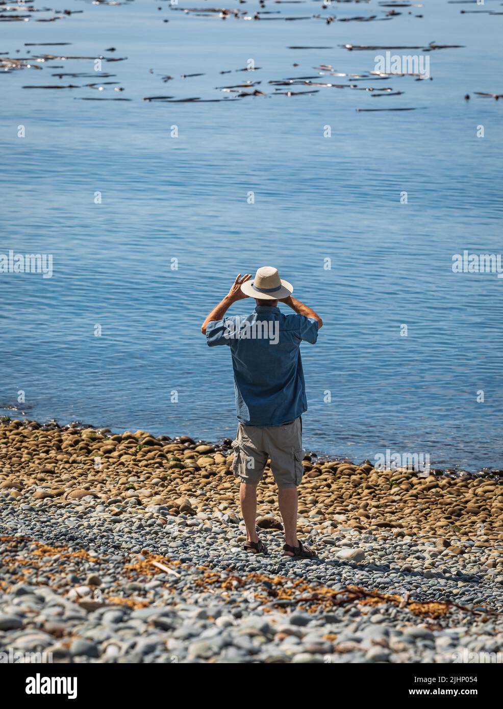 Mann genießt am Strand an einem Sommertag im Urlaub. Mann im Hut macht Fotos mit seinem Smartphone am Strand. Reisefoto, selektiver Fokus Stockfoto