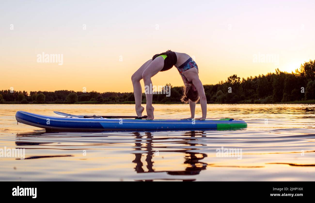Sport Frau Yogini Skorpion Pose Praxis Yoga-Übung auf supboard auf dem Meer in entspannenden Tag, Yoga ist Meditation und gesunde Sport concept.Yoga auf Stockfoto