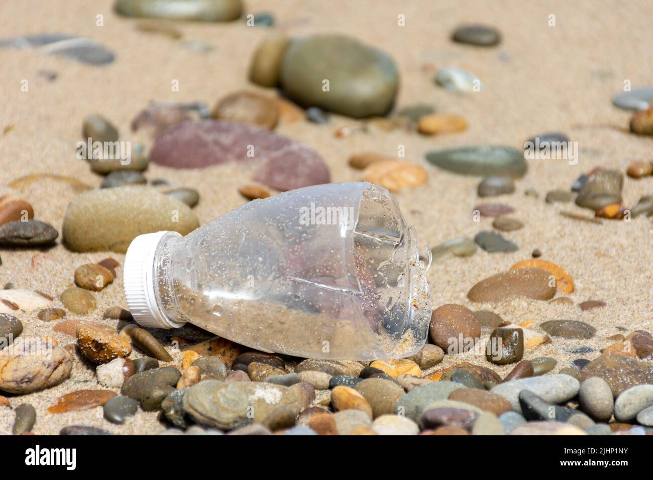 Eine halbe Plastikflasche an einem Kiesstrand. „Save Planet“-Konzept. Stockfoto