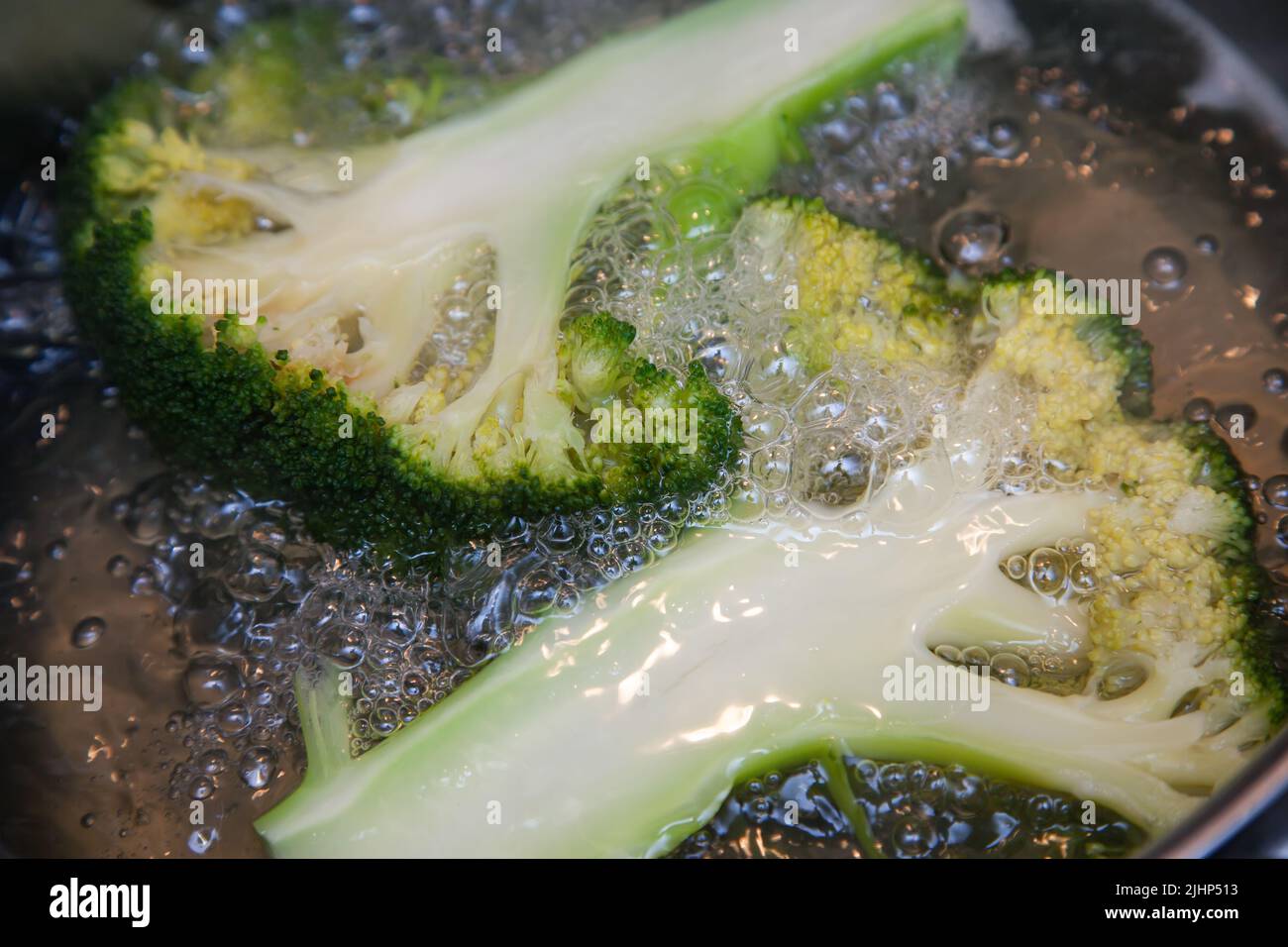 Brokkoli-Blütenstände, längs geschnitten, werden in kochendem Wasser in einem Topf gekocht, aus der Nähe Stockfoto