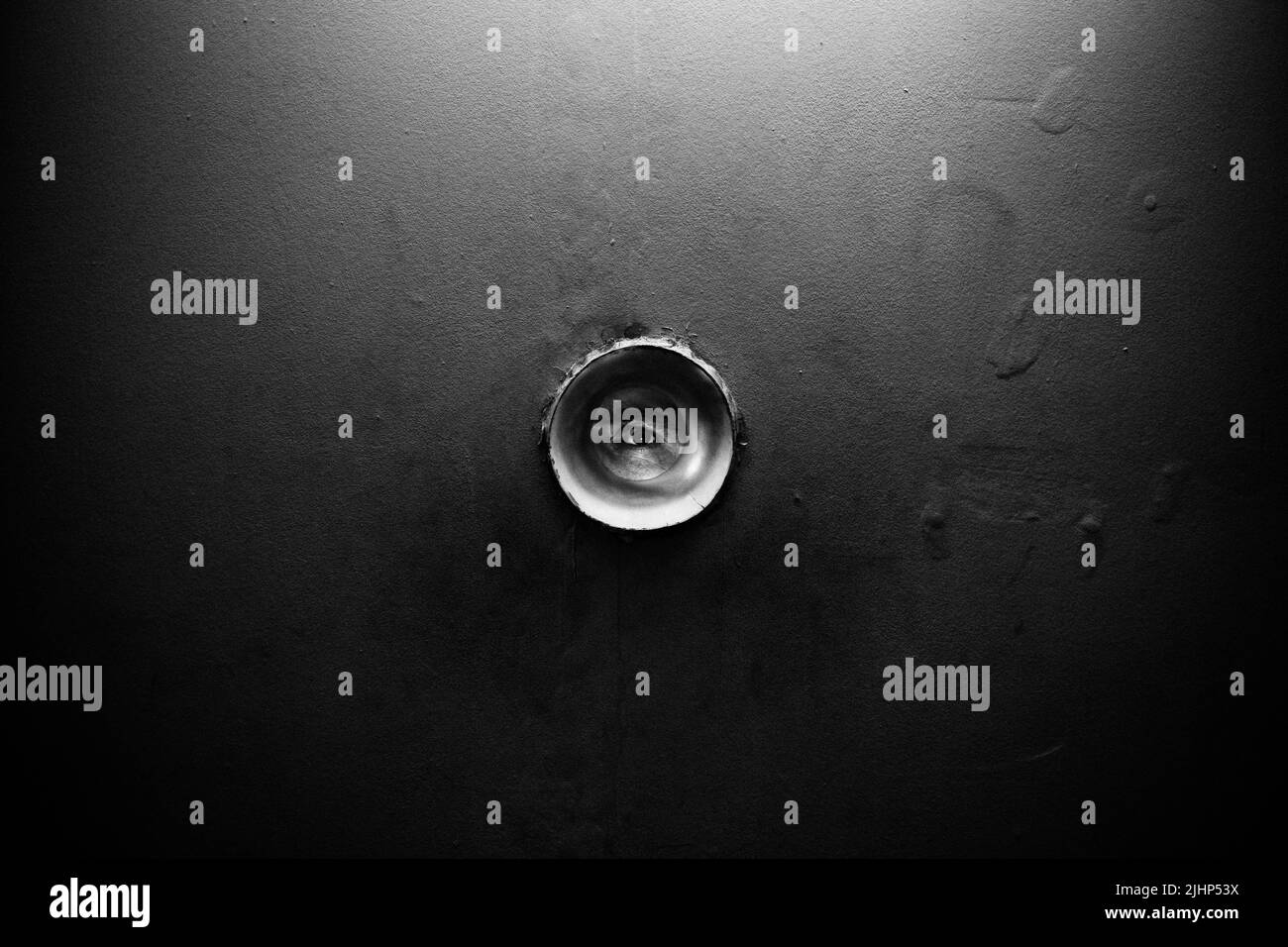 Rundes Loch in der Wand. Durch das Loch ist ein Auge sichtbar. Jemand schaut zu. Sie beobachten und Ihre Geheimnisse ausschnüffeln. Stockfoto