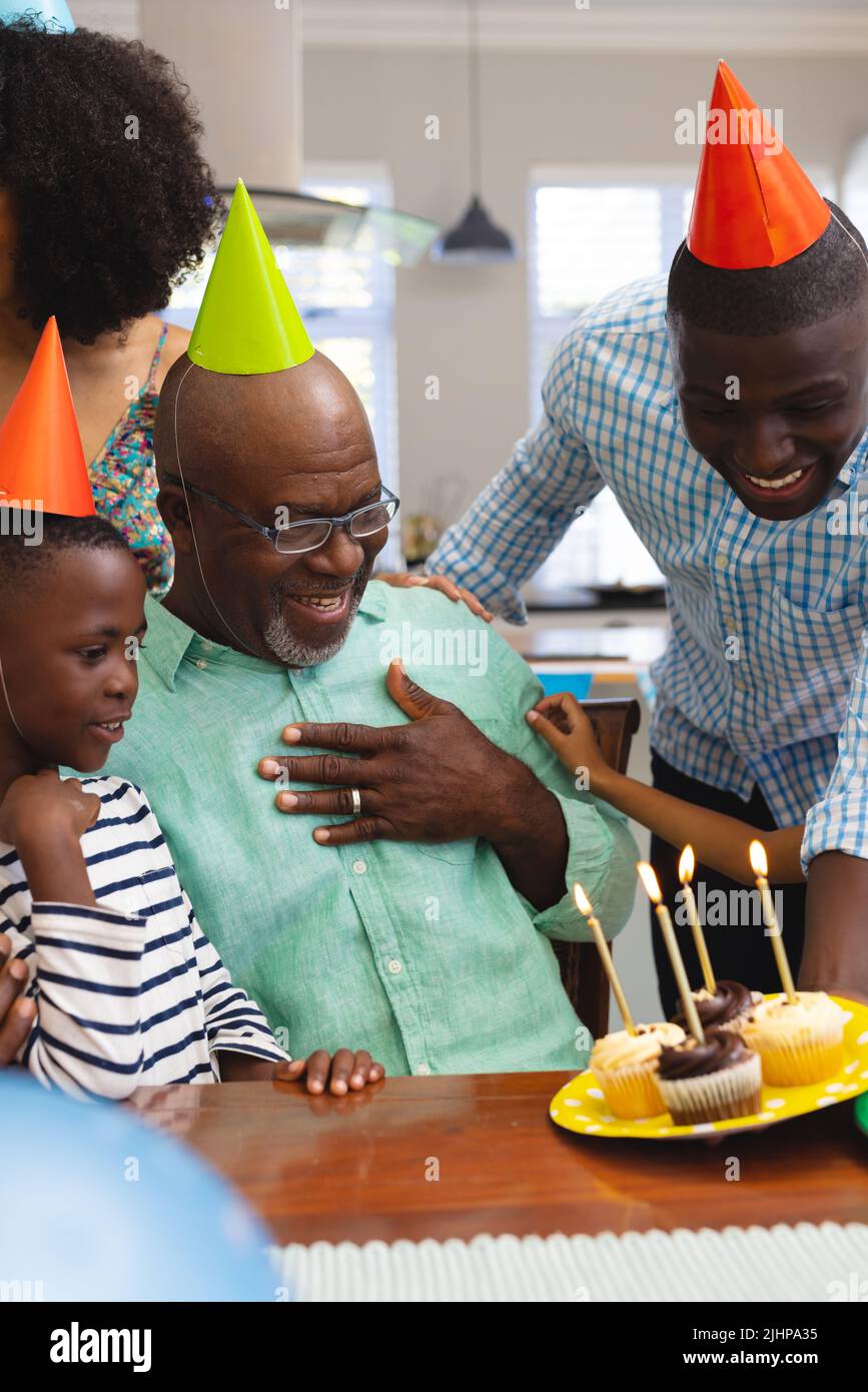 Mehrrassiger älterer Mann mit Partyhut und Blick auf Cupcakes, während er mit der Familie Geburtstag feiert Stockfoto