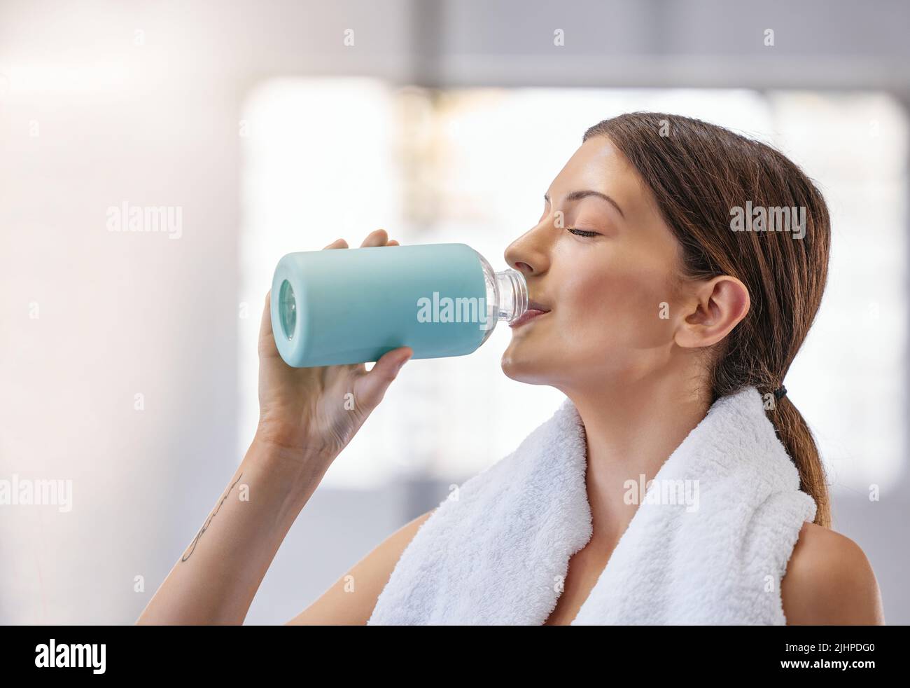 Eine junge kaukasische Frau, die eine Ruhepause einnahm, um Wasser aus der Flasche zu trinken, während sie im Fitnessstudio trainiere. Weibliche Sportlerin, die Durst und Abkühlung stillen Stockfoto