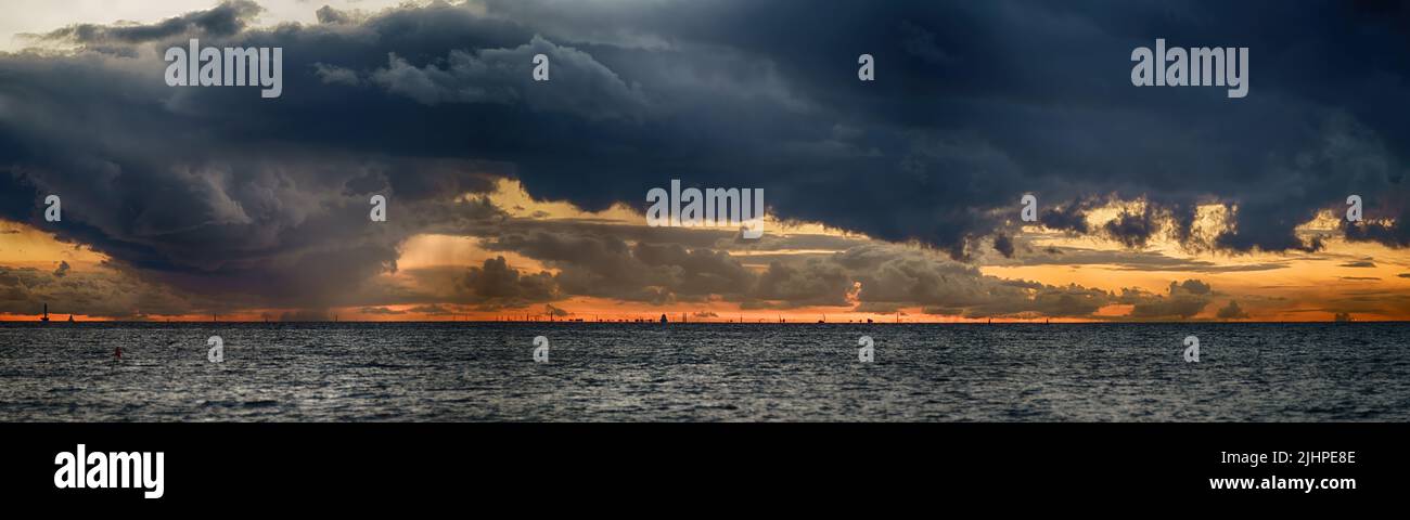 Stürmisches Meer unter dunklem, stürmischem Himmel mit Fata Morgana am Horizont. Große Panorama-Seestücke bei Sonnenuntergang Stockfoto