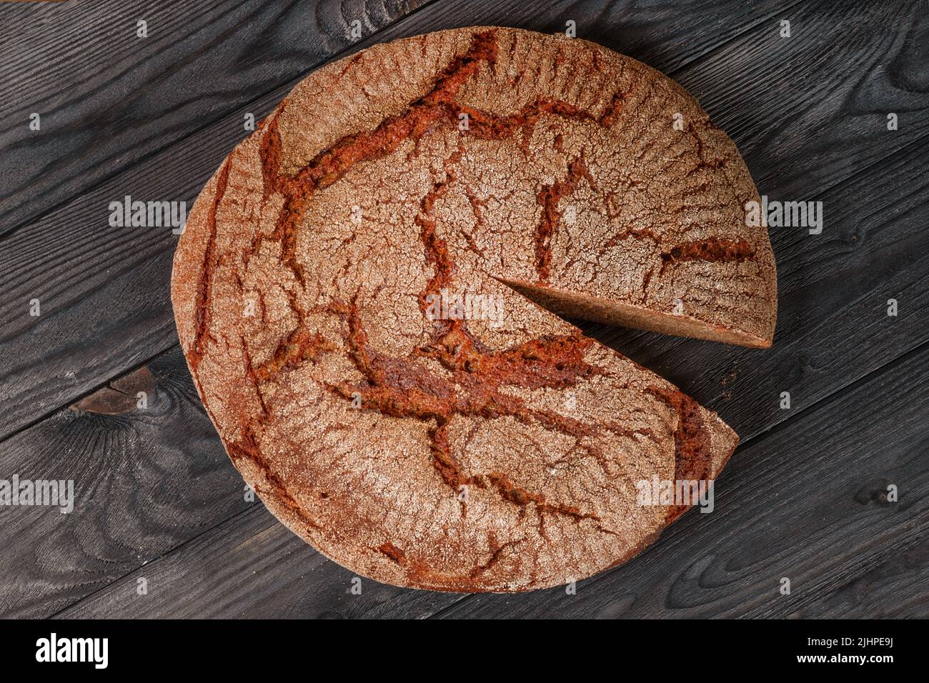 Großer runder Laib Brot mit einem Stück auf schwarzem Holztisch. Dunkles HDR-Foto. Einfache Lebensmittel, magere Lebensmittel, Armut und Unterernährung Stockfoto