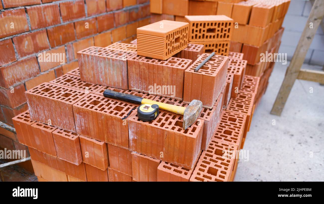 Ein Haufen Ziegelsteine mit Werkzeugen darauf auf der Baustelle eines Wohnhauses. Weitwinkelansicht mit selektivem Fokus Stockfoto