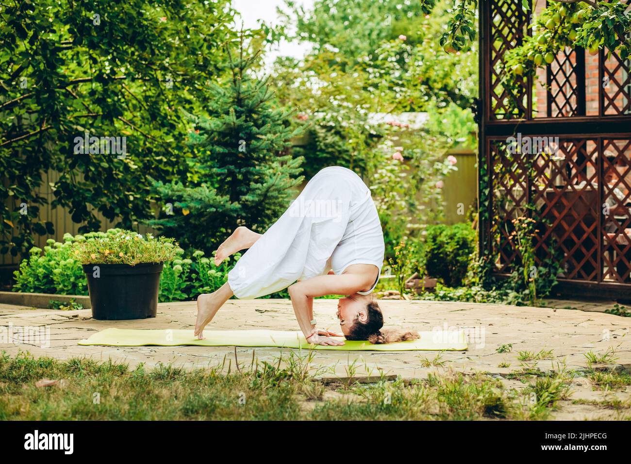 Junge Frau praktiziert Yoga im Hof eines Landhauses. Kopfstand - Ardha Salamba Shirshasana. Stockfoto