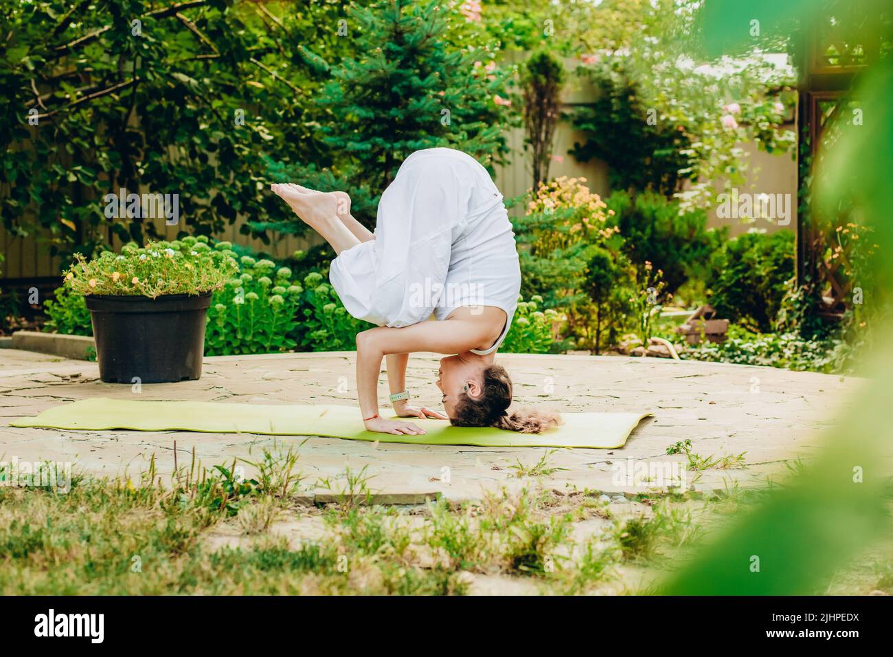 Junge Frau praktiziert Yoga im Hof eines Landhauses. Kopfstand - Ardha Salamba Shirshasana Stockfoto
