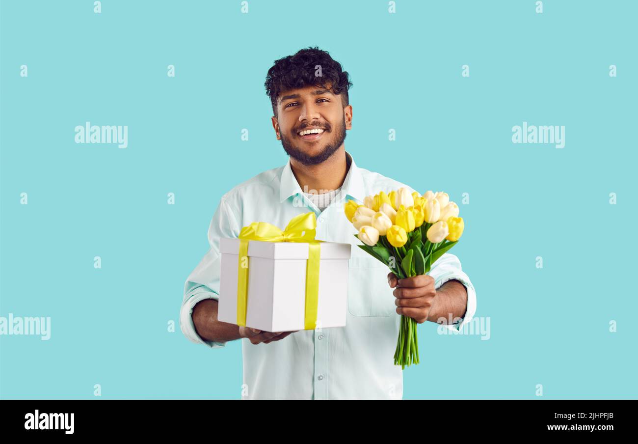 Glücklicher junger Inder hält Blumen und Geschenkbox und gratuliert Liebsten zum Geburtstag oder Urlaub Stockfoto