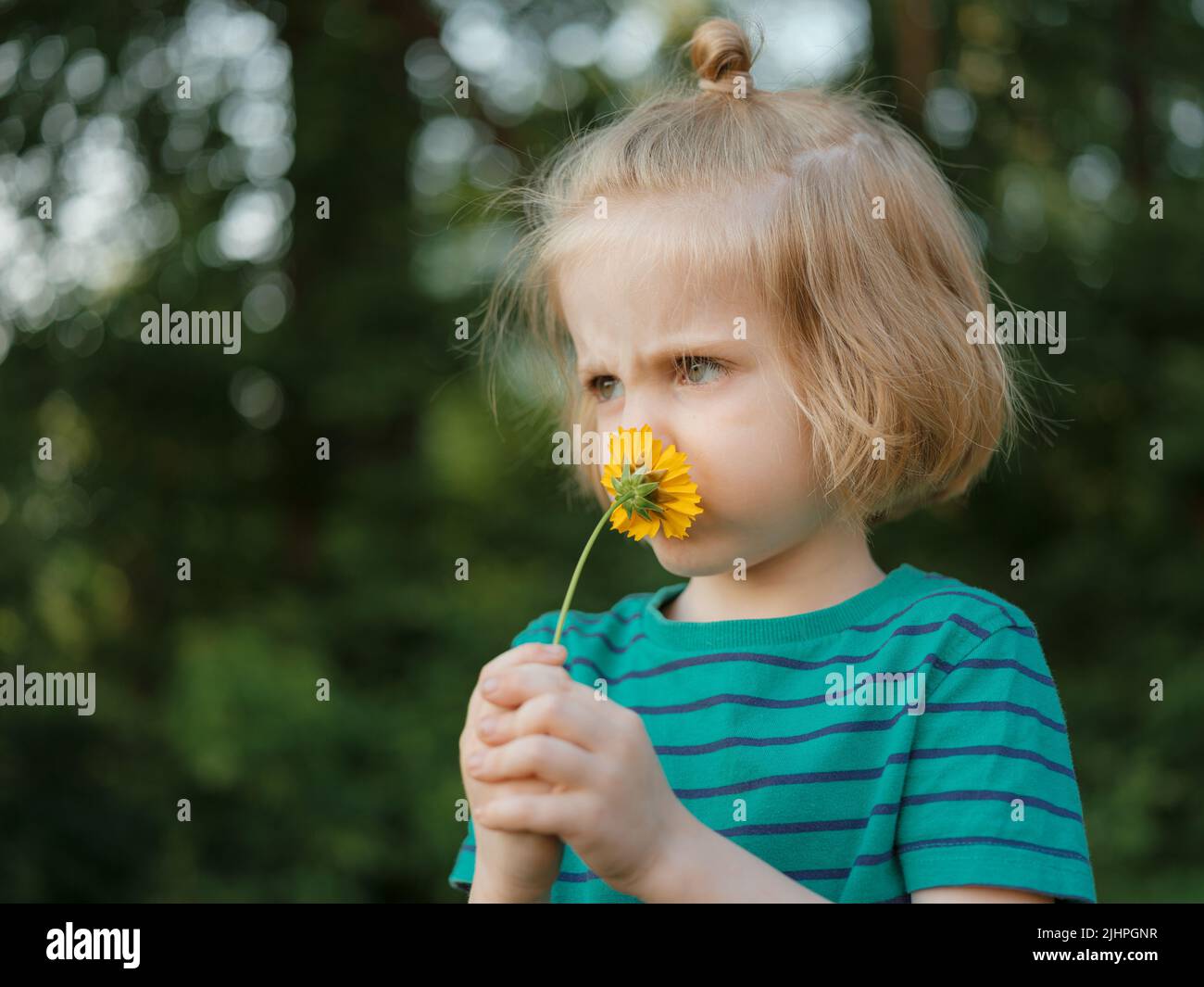 Nahaufnahme Porträt eines kleinen Jungen mit langen blonden Haaren halten und riechende Blume mit gelben Blütenblättern außen Stockfoto