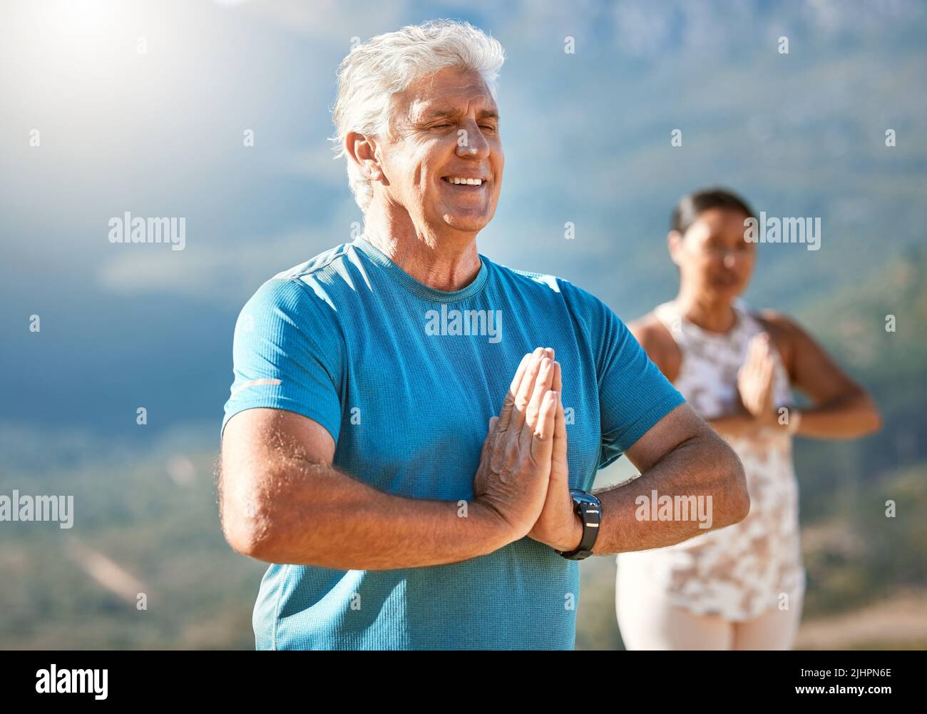Älterer Mann meditiert mit verbundenen Händen und geschlossenen Augen und atmet tief. Reife Menschen, die Yoga in der Natur machen und einen gesunden aktiven Lebensstil leben Stockfoto
