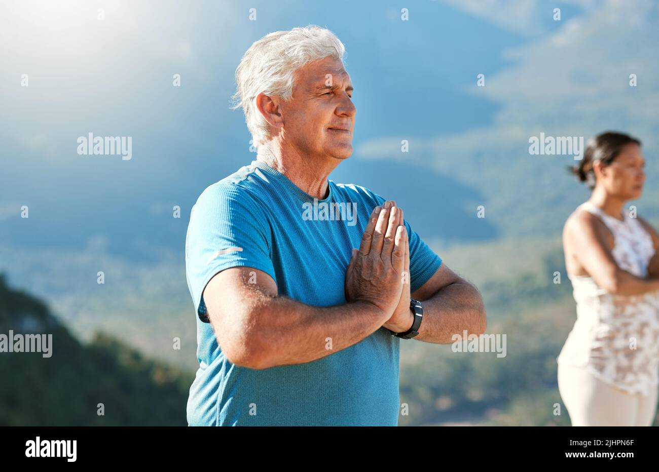 Älterer Mann meditiert mit verbundenen Händen und geschlossenen Augen und atmet tief. Reife Menschen, die Yoga in der Natur machen und einen gesunden aktiven Lebensstil leben Stockfoto