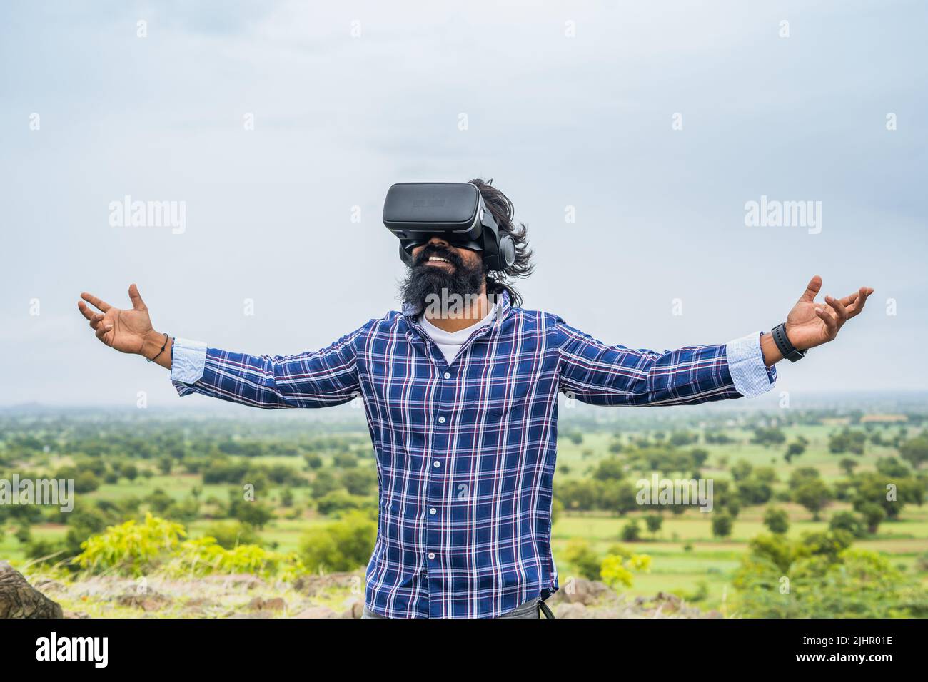 Junger Bartmann, der VR auf Hügelhöhe nutzt, indem er Handgesten auf die Natur anfasst - Konzept der virtuellen Interaktion, Innovation und Unterhaltung. Stockfoto