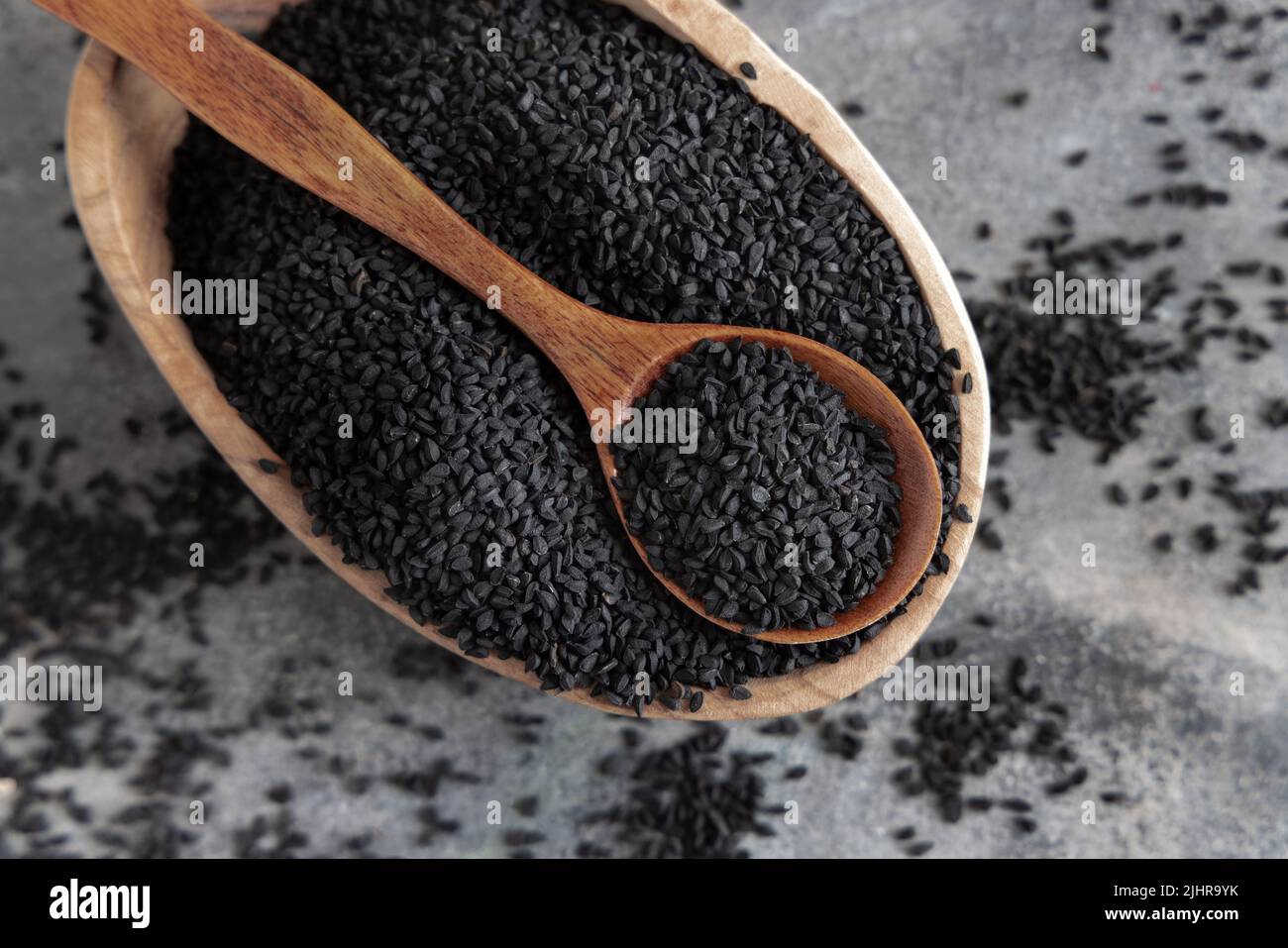 Indische Gewürze Schwarzkümmel (Nigella sativa oder Kalonji) Samen in Schüssel mit Löffel auf grauem Tisch Draufsicht. Traditionelle Medizin, gesunde und vegetarische foo Stockfoto