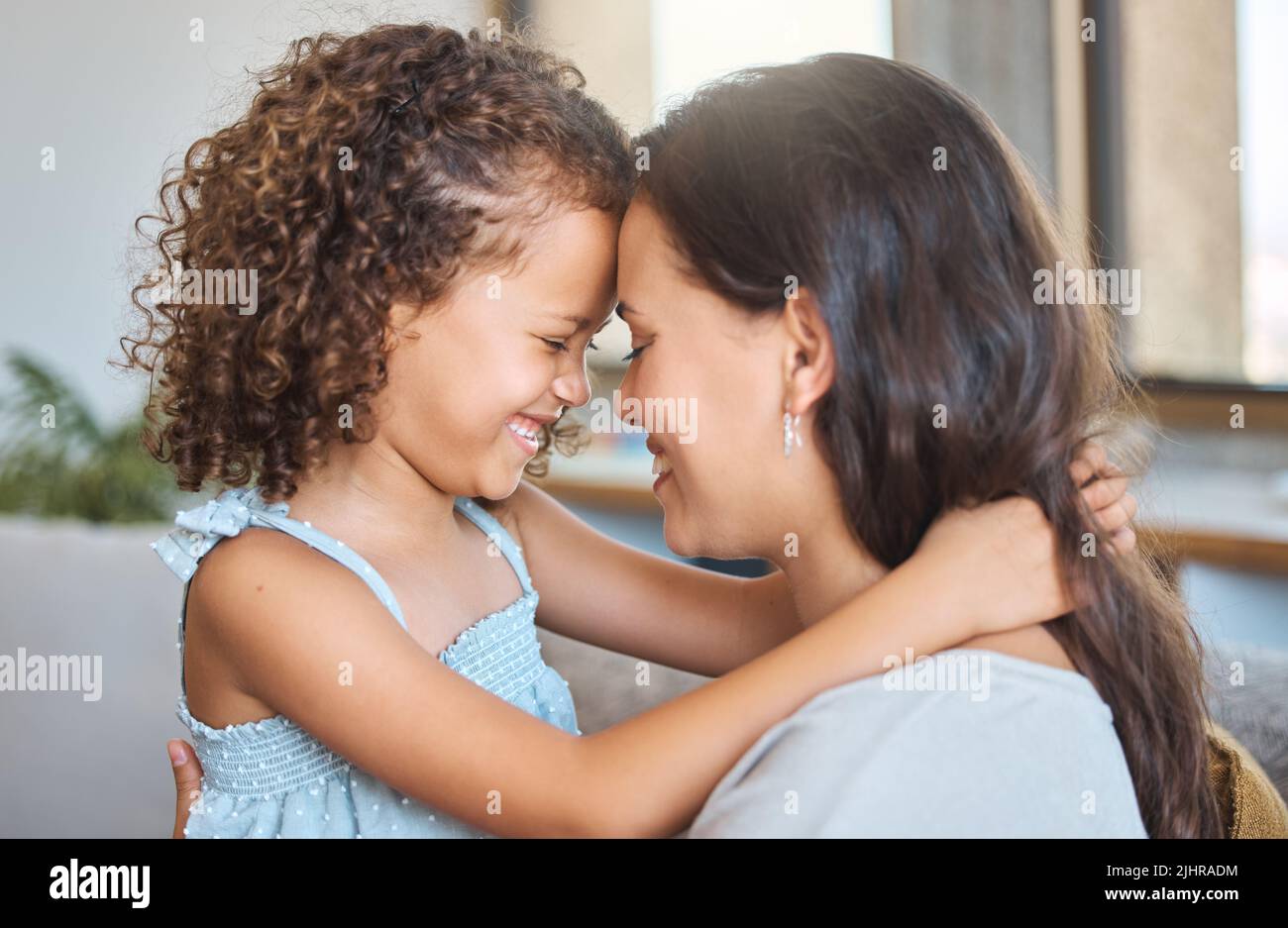 Nahaufnahme von fröhlicher Mutter und Tochter, die einen besonderen Moment teilen, während sie die Stirn berühren und zu Hause von Angesicht zu Angesicht sitzen. Süßer Moment zwischen den Eltern Stockfoto