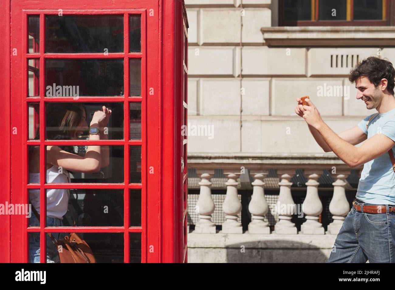 London rief an, wir antworteten: Ein junger Mann, der mit seinem Smartphone in einer Telefonzelle Fotos von seiner Freundin machte, während er die Stadt London erkundete. Stockfoto