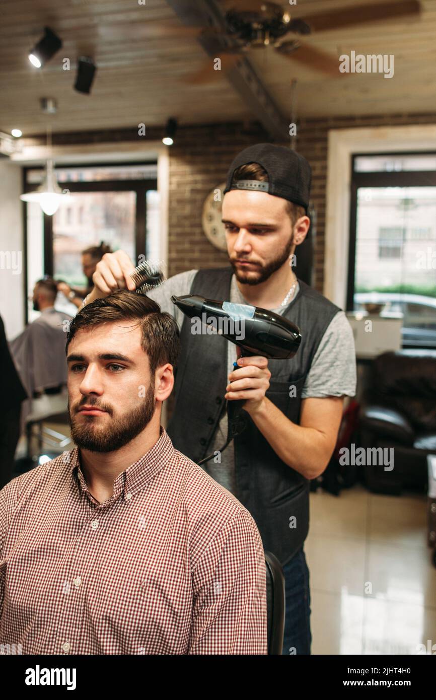 Stylistin macht moderne Frisur für jungen Mann Stockfoto