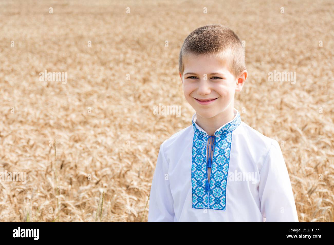 Weiche selektive Fokussierung eines Schuljungen in einer bestickten Jacke auf einem agro-industriellen Feld eines Weizenfeldes an einem sonnigen Tag. Das Kind lächelt aufrichtig. Unabhängigkeitstag, Verfassung der Ukraine. Stockfoto