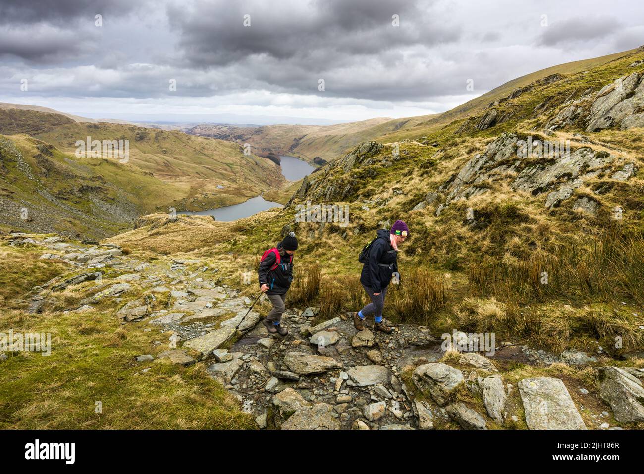 Zwei Wanderer steigen auf den Nan Bield Pass mit dem Small Water Tarn und dem Haweswater Reservoir unten im Lake District National Park, Cumbria, England. Stockfoto