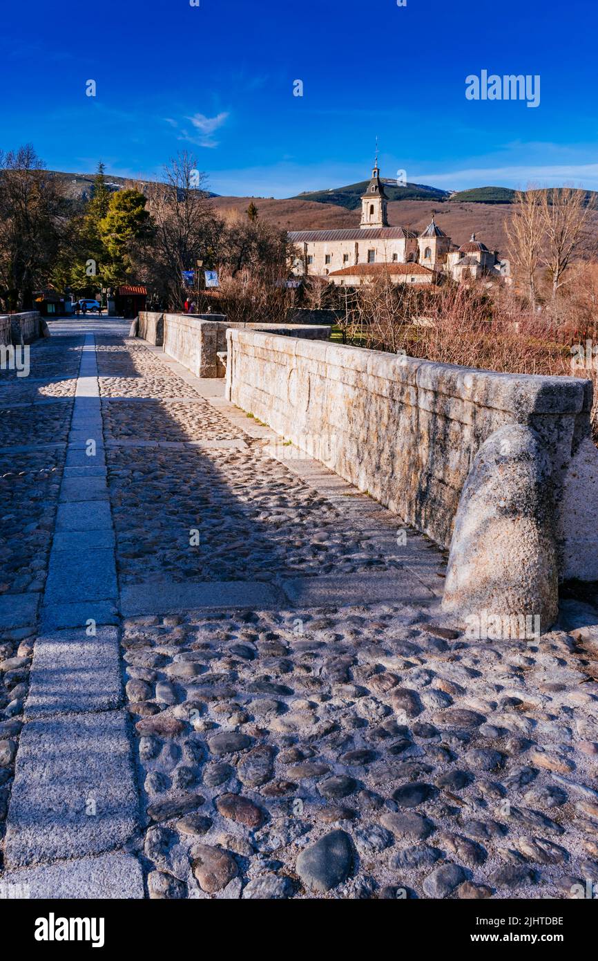 Die Puente del Perdón - Brücke der Begnadigung, ist eine steinerne Brücke über den Fluss Lozoya. Im Hintergrund das Monasterio de Santa María de El Paular - Stockfoto