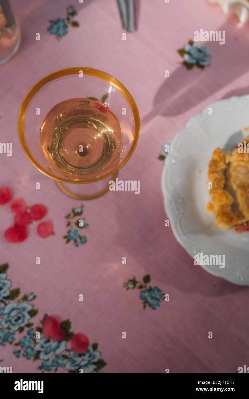 Goldrand Glas Roséwein auf rosa Tischdecke mit blauen Rosen, Rhabarberpastete an der Seite Stockfoto