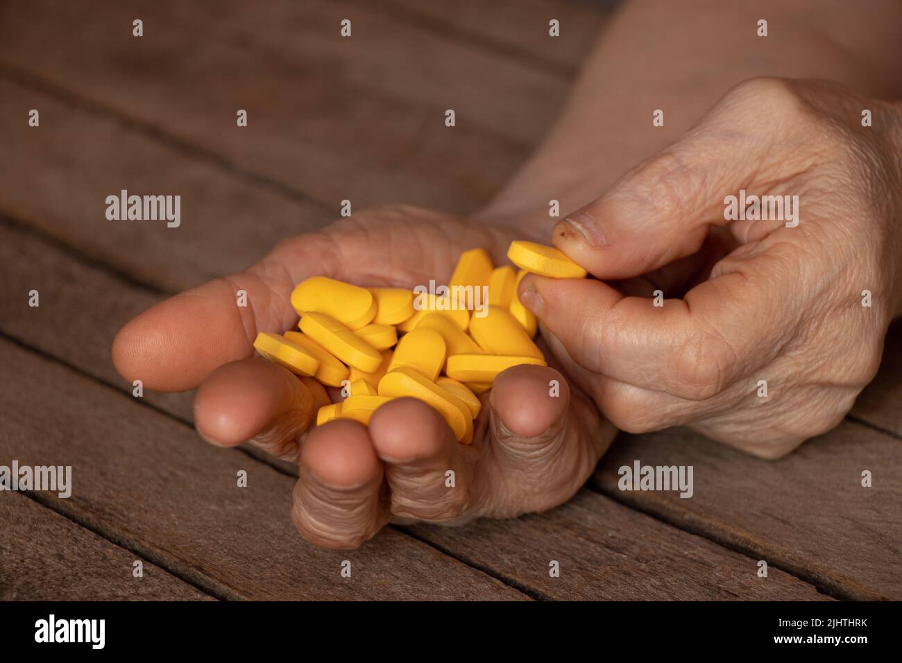 Großmutter hält gelbe Pillen in den Händen auf einem Holztisch, Pillen in den Händen und Frauen liegen und Medizin Stockfoto