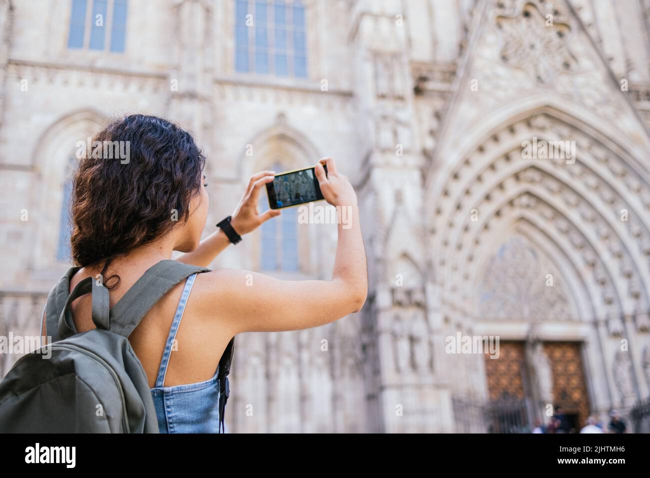 Junge Brünette mit Rucksack fotografieren mittelalterliche Kathedrale per Smartphone, während die Straßen der historischen Stadt tagsüber erkunden Stockfoto