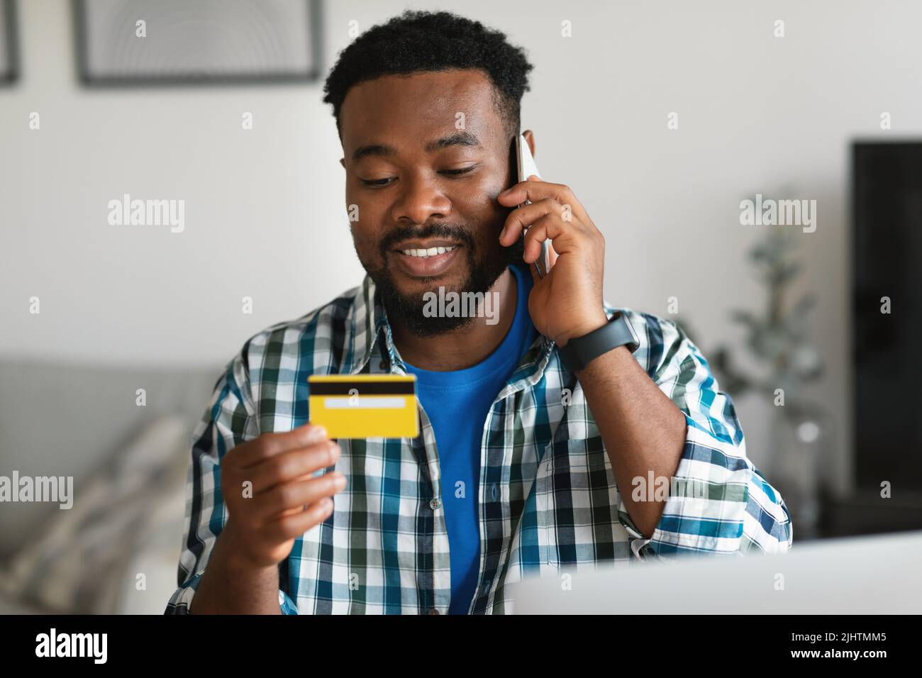 African Man Holding Credit Card Talking On Cellphone At Workplace Stockfoto