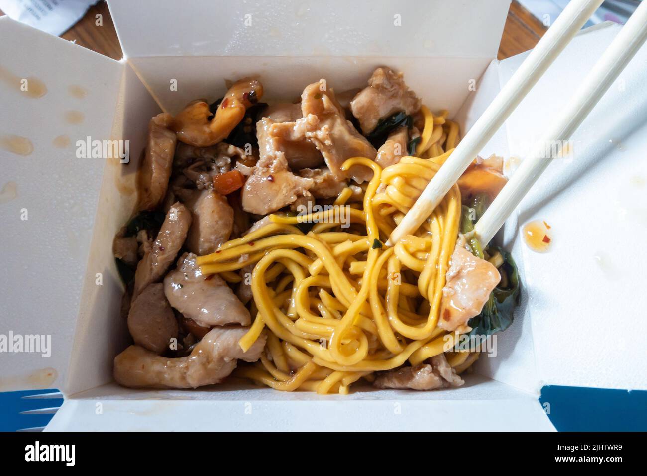 Essen Sie eine chinesische Mahlzeit zum Mitnehmen mit süßem und saurem Schweinefleisch mit Eiernudeln und verwenden Sie Essstäbchen. Stockfoto