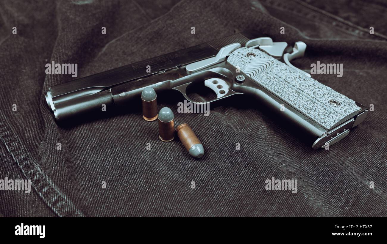 Pistole des Modells 1911 und drei Patronen (.45 ACP) auf schwarzem Denim-Hintergrund Stockfoto