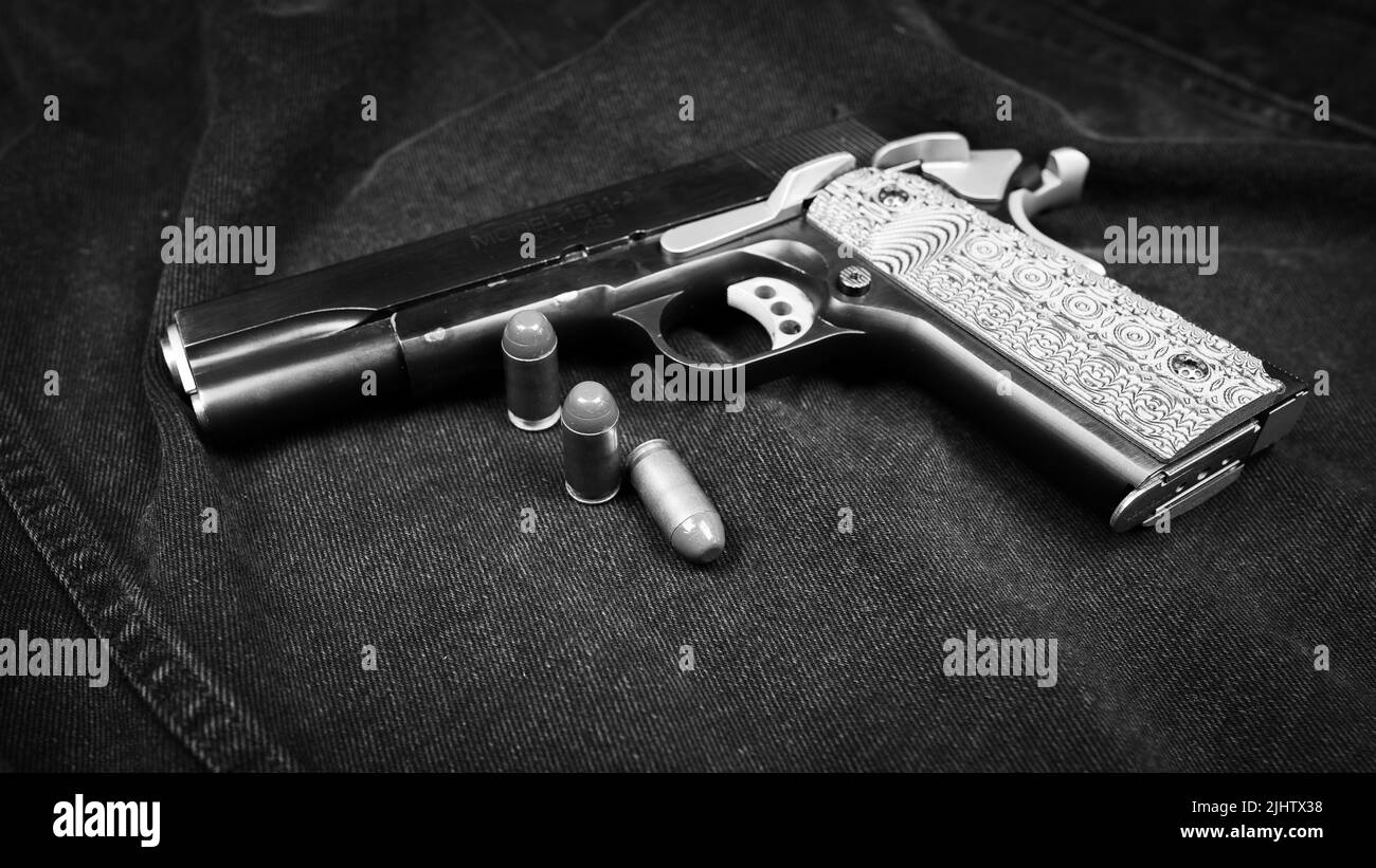 Modell 1911 Pistole und drei Patronen (.45 ACP) auf schwarzem Denim-Hintergrund, monochromes Foto Stockfoto