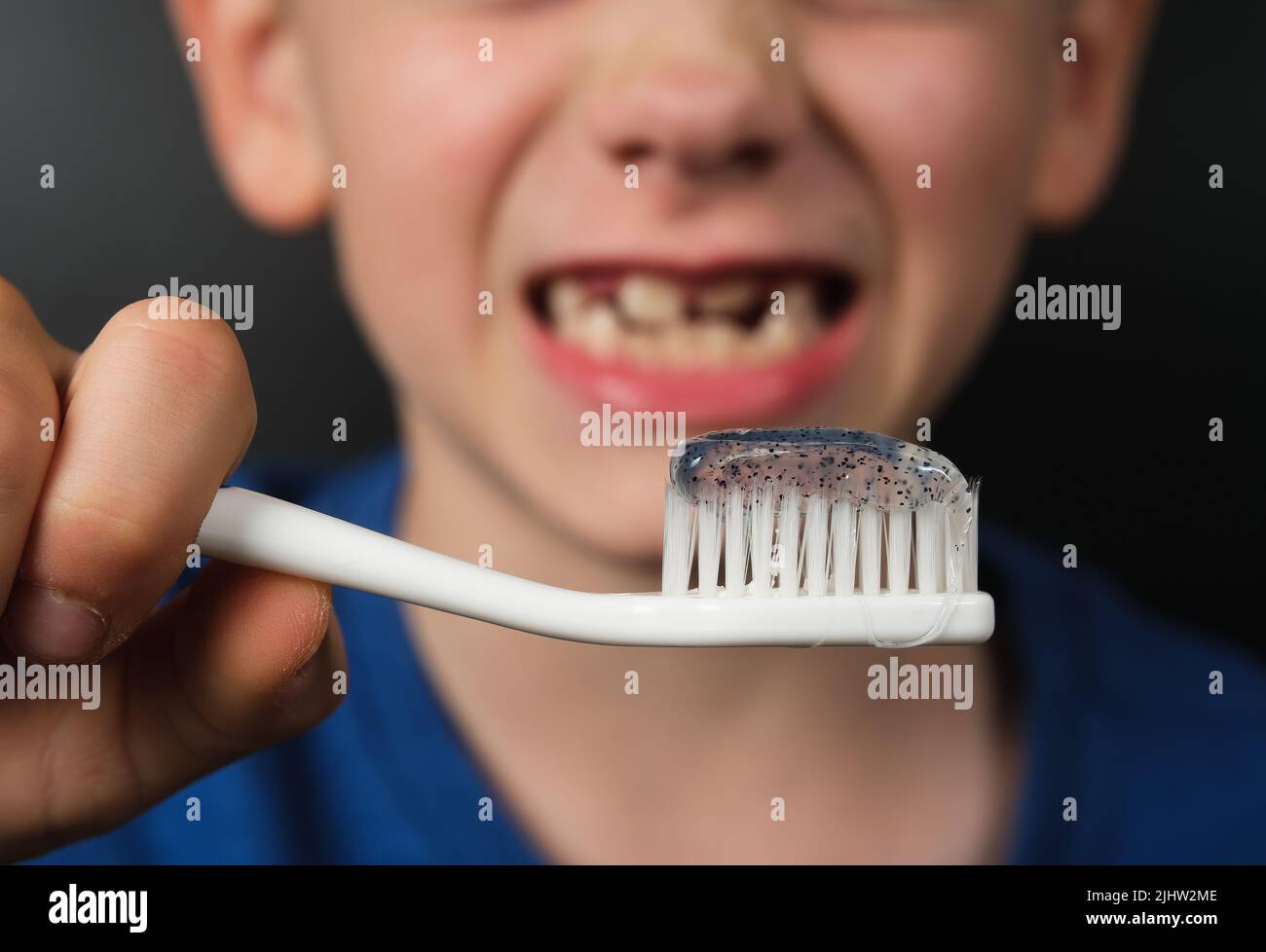 Zahnbürste mit Zahnpasta in den Händen eines 8 Jahre alten lächelnden Kindes, ohne Zähne. Konzept für Körperpflege und Hygiene. Stockfoto