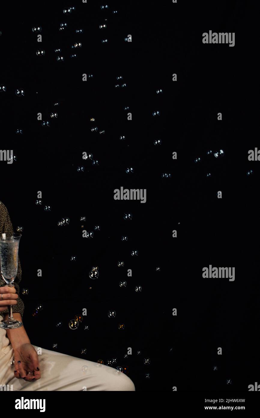 Blasen schweben auf schwarzem Hintergrund, Frau mit Sektflöte aus funkelndem Wasser Stockfoto