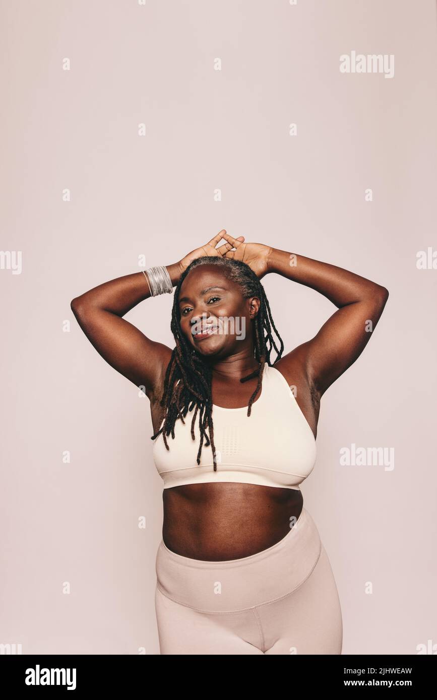 Eine sportliche Frau, die vor grauem Hintergrund auf die Kamera blickt. Reife Frau mit Dreadlocks in Sportkleidung in einem Studio. Mittel- Stockfoto