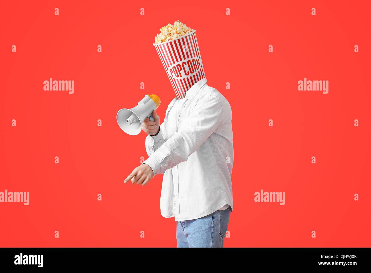 Junger Mann mit einem Eimer aus knusprigem Popcorn anstelle seines Kopfes und einem Megaphon auf rotem Hintergrund Stockfoto
