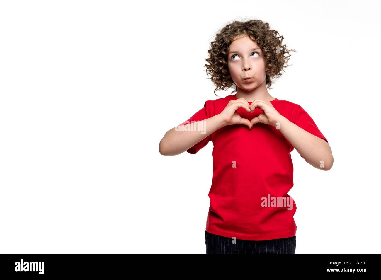 Freundliche сurly kurzhaarige weibliche Kind Mädchen 10-12 Jahre alt trägt rote Basic-T-Shirt. Lustige präteen Schulmädchen zeigt Herzform aus zwei Händen wieder Stockfoto