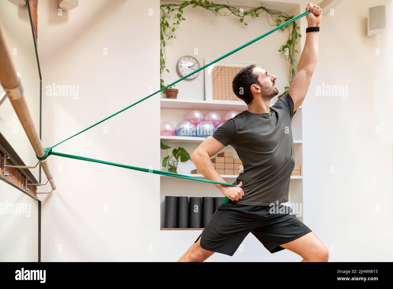 Seitenansicht eines sportlich starken Mannes im aktiven Ohr, der während des intensiven Trainings in einem leichten modernen Fitnessstudio mit Widerstandsbändern trainiert Stockfoto