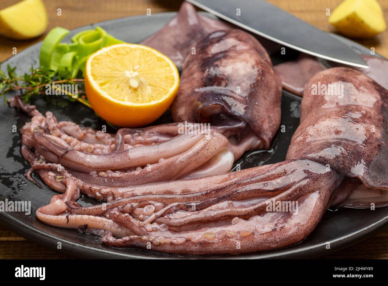 Frischer Tintenfisch mit Tentakeln, Zitrone und Messer auf schwarzem Teller. Nahaufnahme. Draufsicht Stockfoto