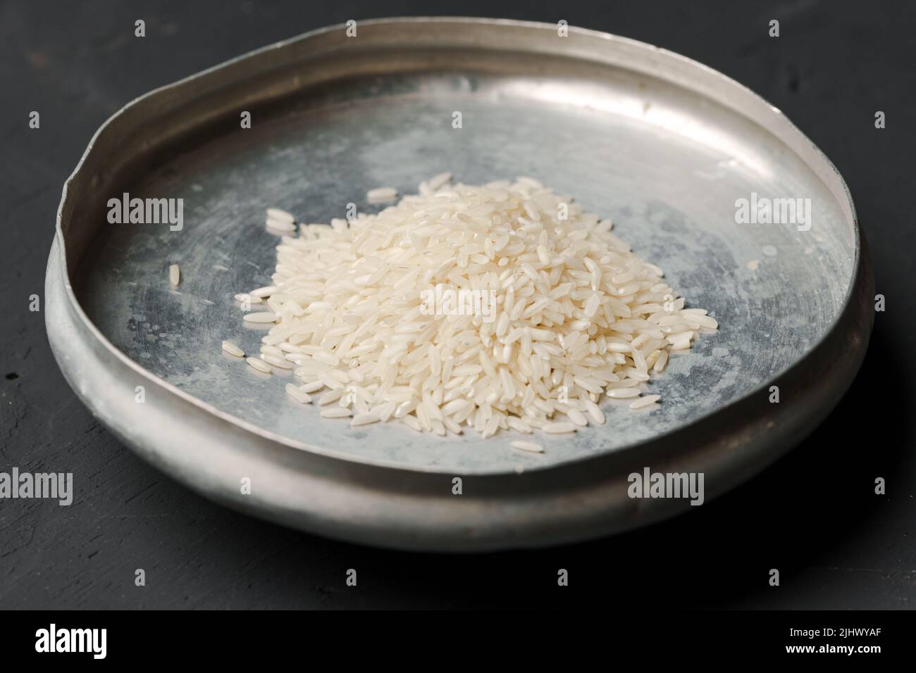 Haufen von trockenem Reis in einer Schüssel auf schwarzem Hintergrund, Mangel an Nahrung, Hunger-Konzept Stockfoto