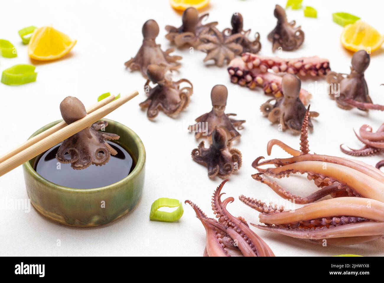 Kleine Krake auf Bambusstäbchen in Schüssel mit Sojasauce. Gekochte Tintenfisch-Babys und Tintenfische mit Tentakeln auf dem Tisch. Draufsicht. Weißer Hintergrund Stockfoto
