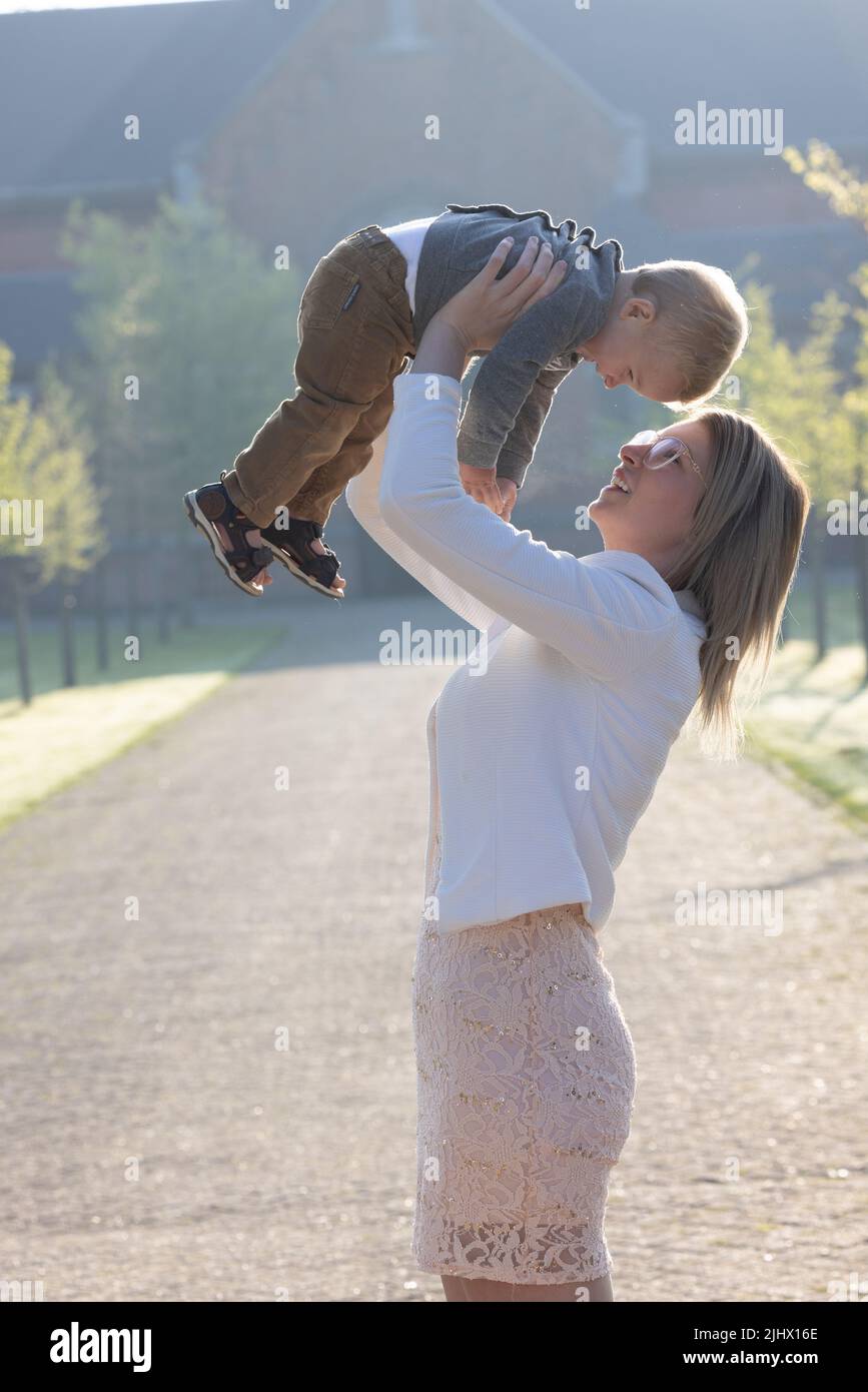Eine junge und glückliche Mutter und ein Kind, spielend, stehen inmitten eines Parks in den Strahlen der aufgehenden Morgensonne. Hochwertige Fotos Stockfoto
