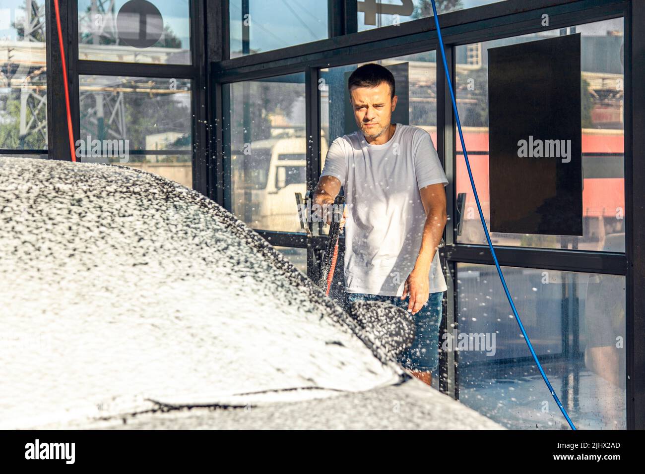 Autowäsche zur Selbstbedienung. Ein Mann wässern sein Auto mit Schaum aus einem Druckschlauch. Stockfoto